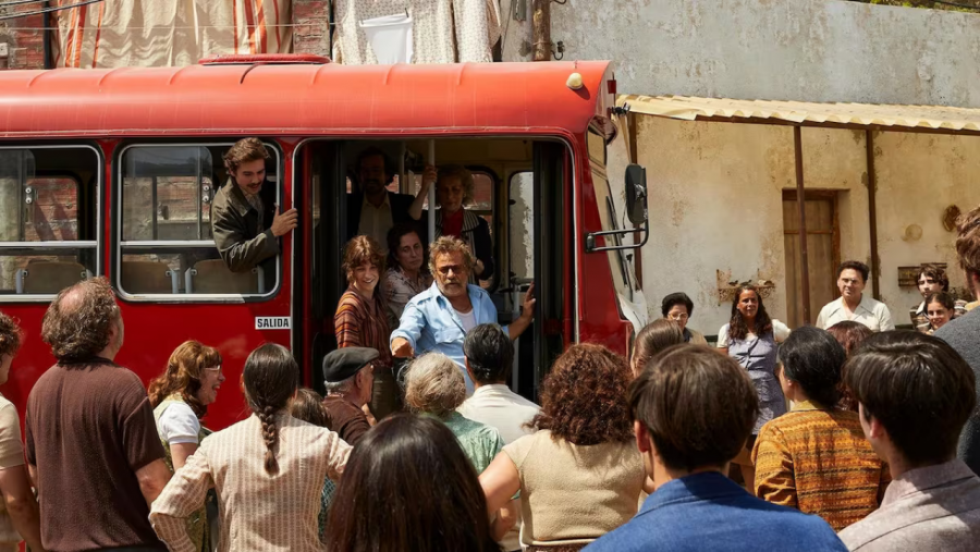 Antiguo autobús rojo con personas alrededor, algunas dentro y otras fuera, mostrando emociones diversas en una escena de despedida o bienvenida.