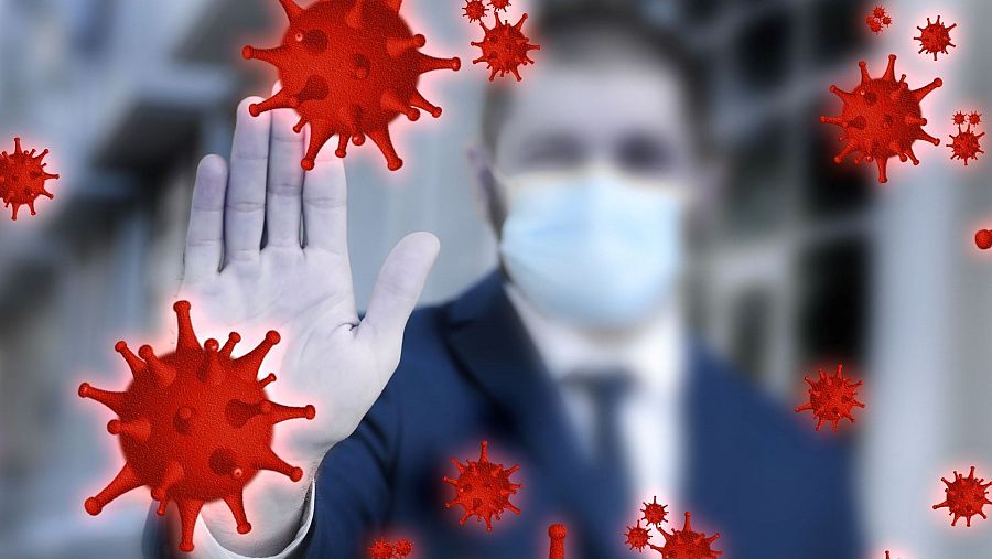 Persona con mascarilla bloquea con la mano varios virus rojos.  Representación visual de la lucha contra una infección viral.