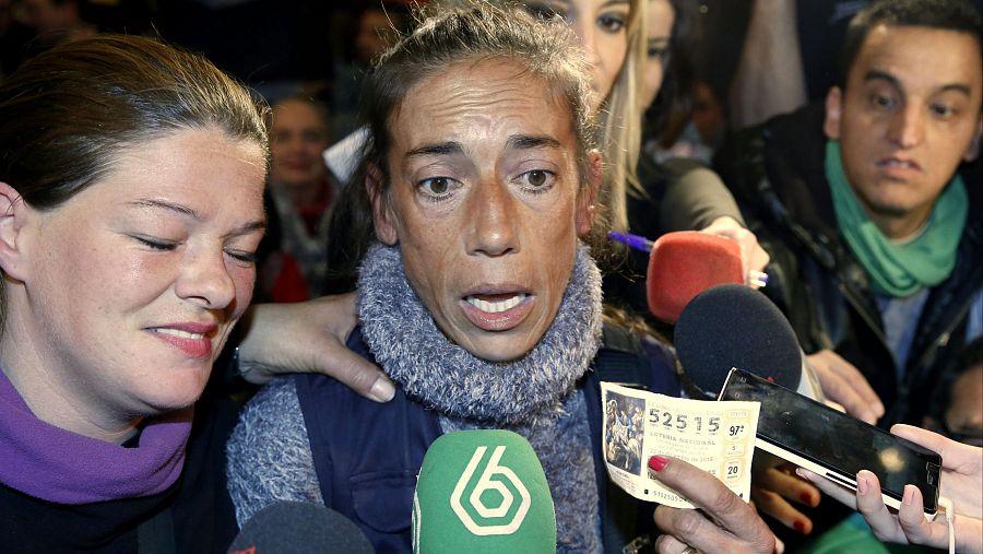 Mujer emocionada muestra décimo de lotería número 52.515 en entrevista rodeada de micrófonos y personas.  Expresión facial impactante.