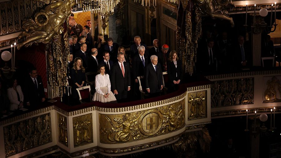 Felipe VI, Letizia y Sergio Mattarella en un palco con decoración dorada, vestidos formalmente, junto a otras personas.  Ambiente elegante y evento importante.