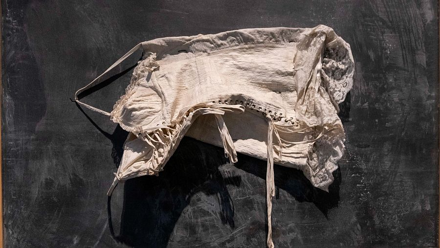 Corpiño o vestido antiguo, color blanquecino con encaje, sobre fondo oscuro.  Desgastes visibles, iluminación que resalta texturas.