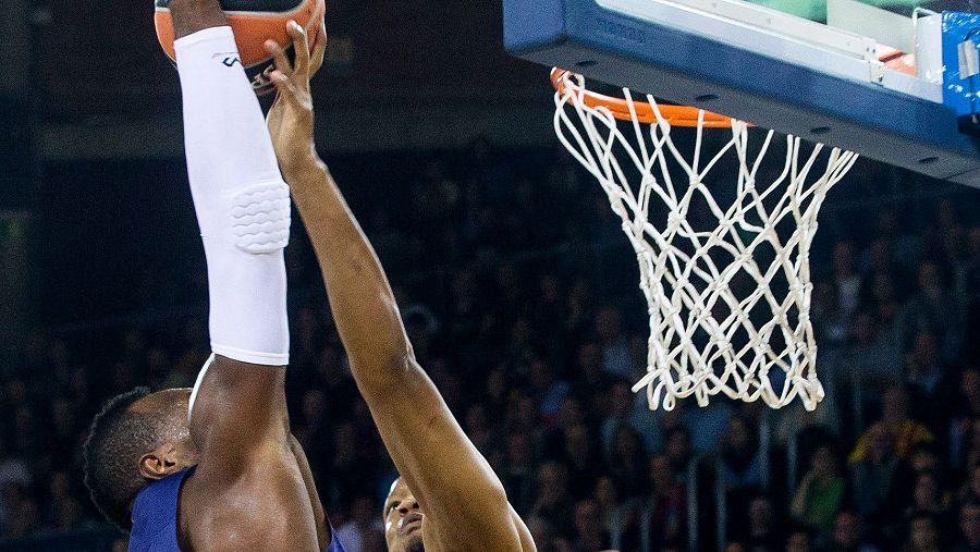 Tapón espectacular de Randolph a Dorsey durante un partido de baloncesto.  Acción aérea cerca de la canasta, con Randolph usando una manga blanca y codera.