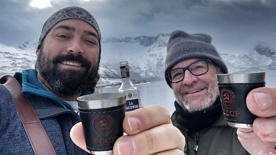 Dos hombres brindan con vodka en un paisaje nevado.