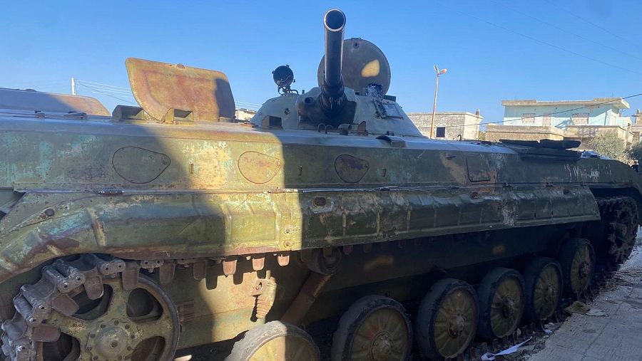 Vehículo militar deteriorado en zona urbana.  Contexto de conflicto e inquietud, según texto adjunto.