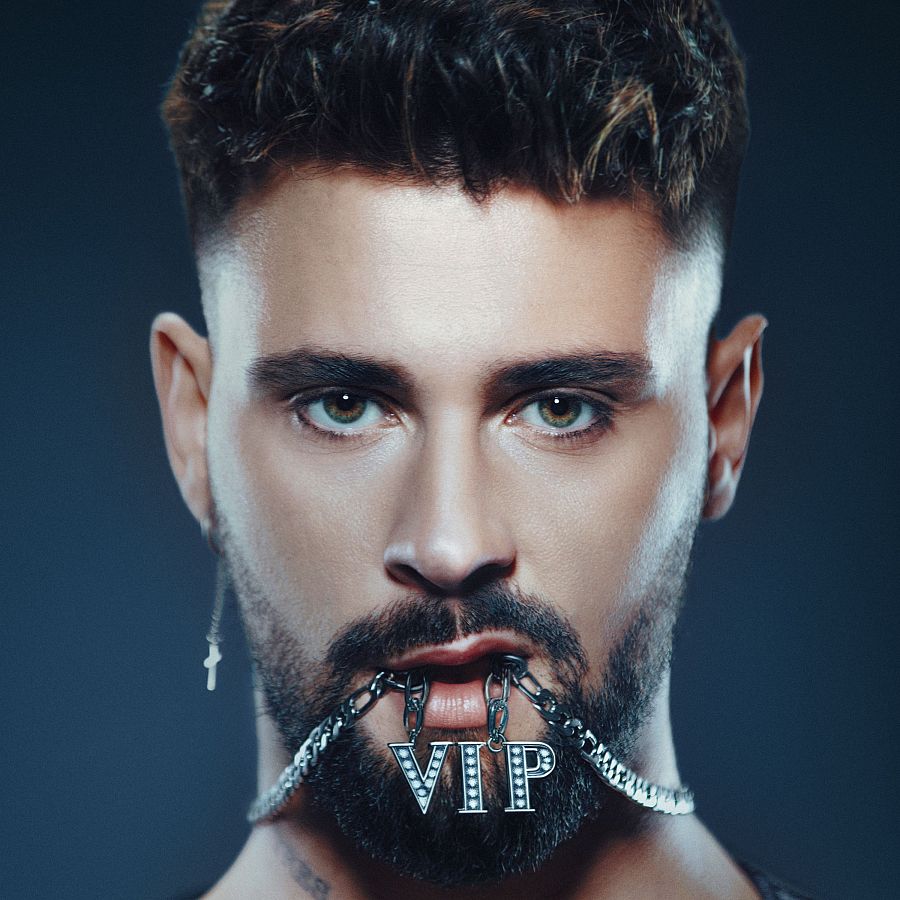 Primer plano de J Kbello sosteniendo una cadena con un colgante 