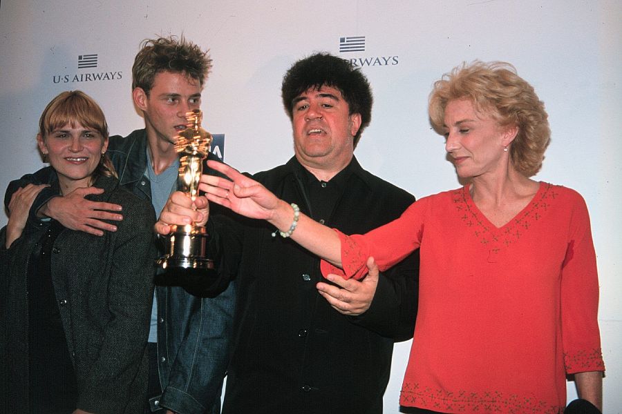 Cuatro actores celebran un premio, mostrando alegría.  Uno sostiene una estatuilla dorada. El fondo es blanco con logotipos.