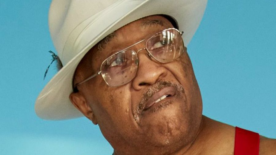 Retrato de un hombre mayor con sombrero blanco y gafas, expresión pensativa.  Posiblemente una imagen promocional relacionada con música.