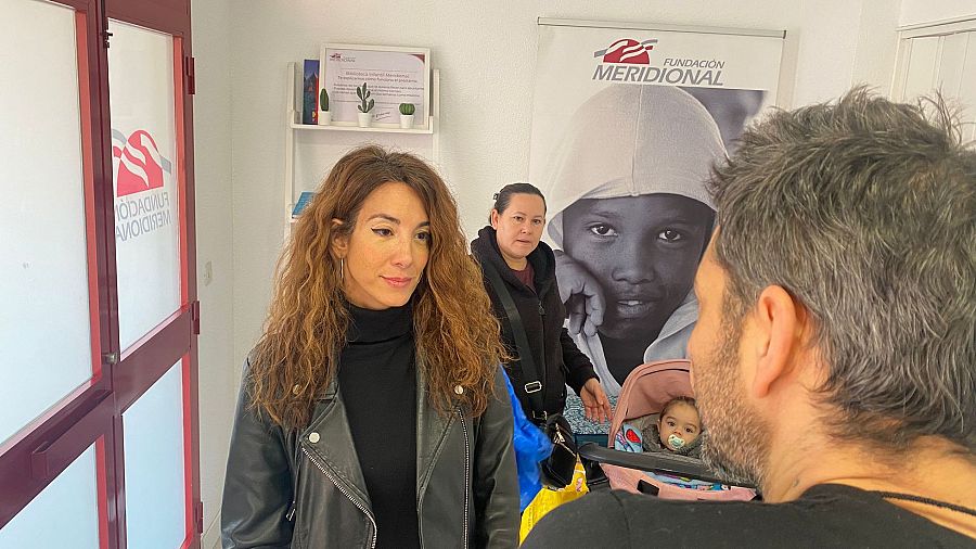 Silvia Saura, con chaqueta negra, y David Cortijo en la Fundación Meridional.  David interactúa con un bebé en un carrito; otra mujer está presente.