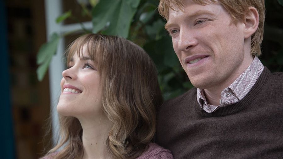 Escena de 'Una cuestión de tiempo' con Rachel McAdams y Domhnall Gleeson, quienes miran hacia arriba con alegría. Él viste un jersey marrón oscuro y ella una prenda rosa malva.