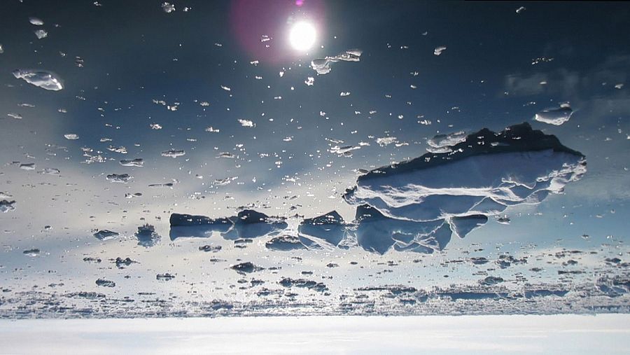 Imagen de paisaje polar con sol brillante reflejado en superficie helada, mostrando trozos de hielo dispersos y una perspectiva baja.