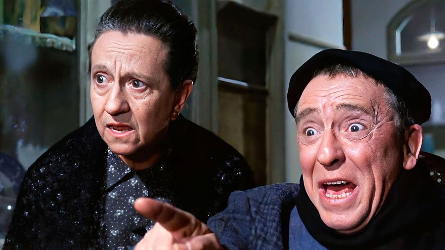 Paco Martínez Soria, con boina, mira sorprendido mientras una mujer con blusa oscura de lunares le señala.  Primer plano de ambos en una escena interior.