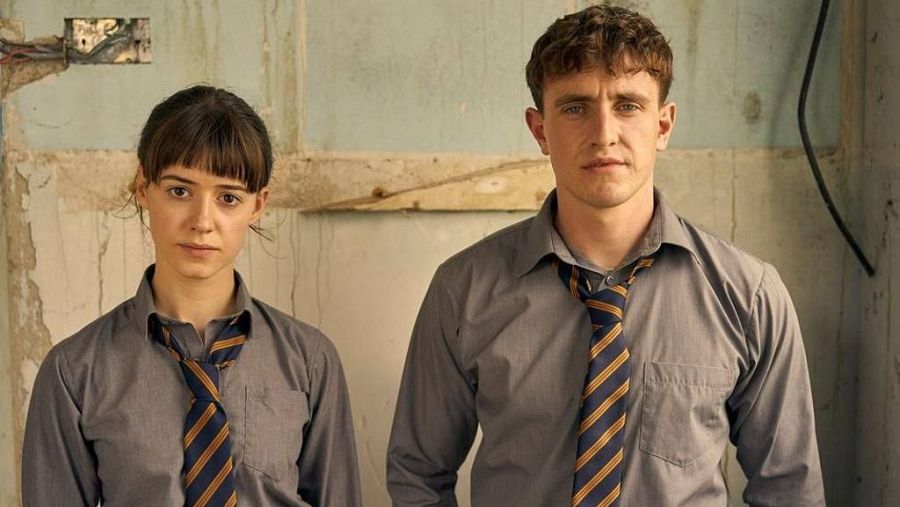 Imagen promocional de 'Normal People' en RTVE Play.  Muestra a dos actores con uniformes escolares, expresiones serias y un fondo desgastado.
