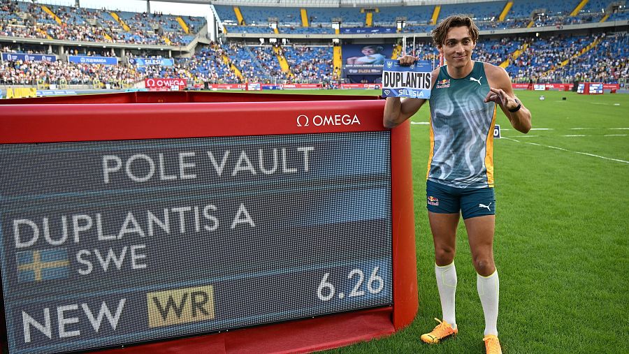 Armand Duplantis celebra su nuevo récord mundial de salto con pértiga (6.26m) junto a un marcador, vistiendo camiseta verde y azul.  El cartel que sostiene menciona Silesia.