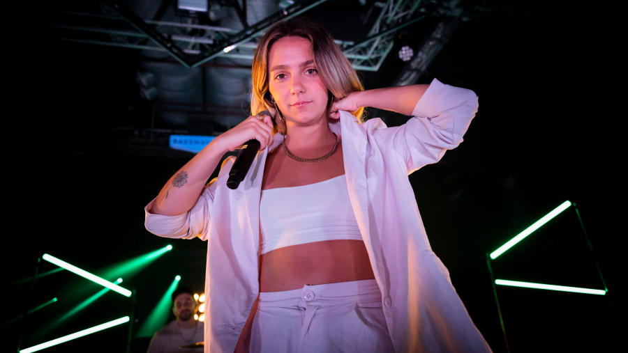 Cantante con atuendo blanco y micrófono en mano, en escenario con iluminación verde. Imagen promocional de TVE Catalunya.