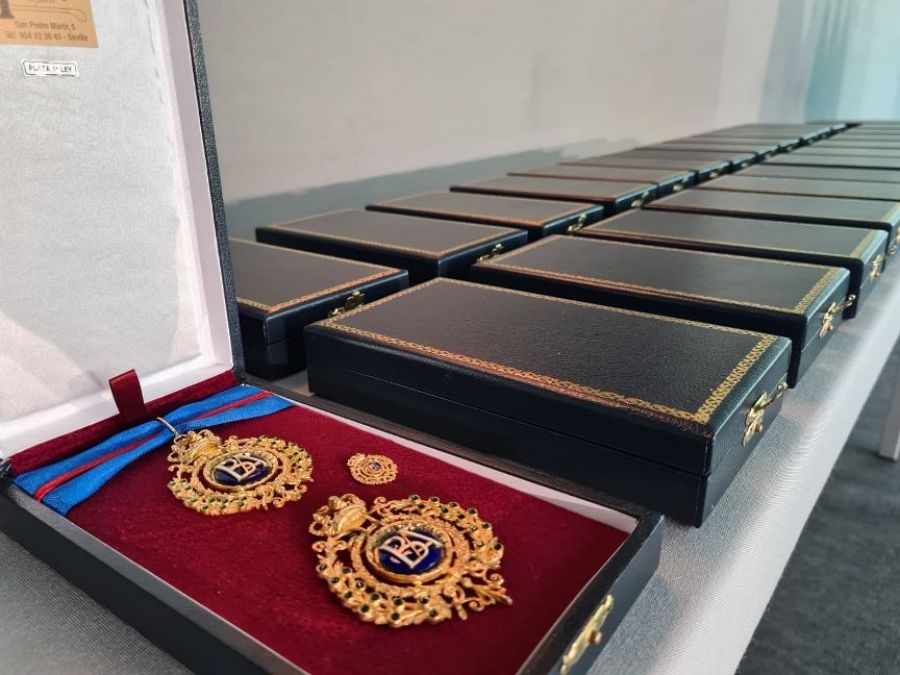 Cajas negras con bordes dorados contienen medallas doradas con detalles azules y letras 