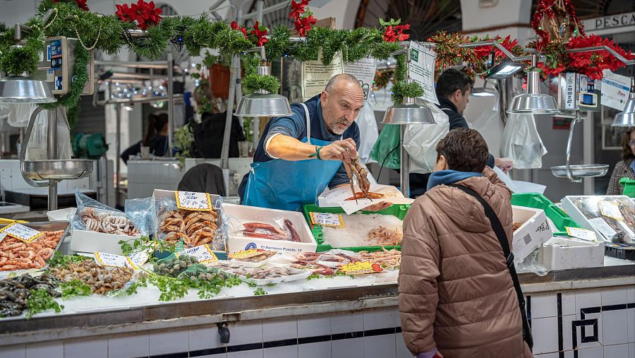 Puesto de pescado navideño: pescadero muestra marisco a clienta.  Pescado, marisco y decoración festiva en un mercado.