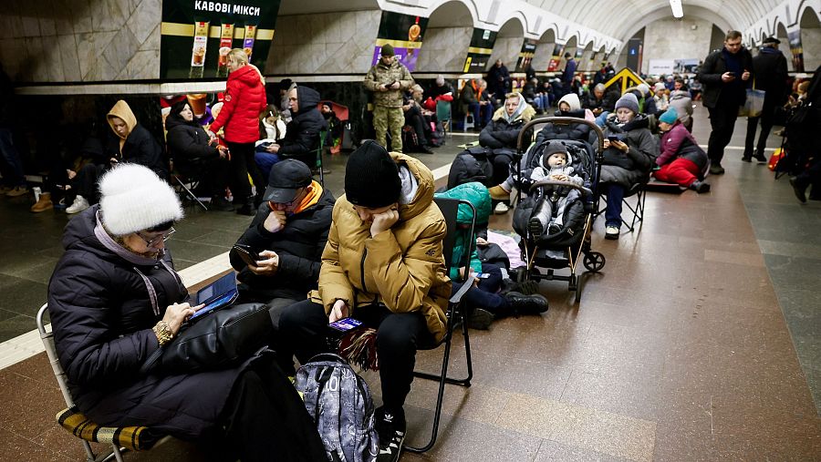 Refugio en estación de metro: civiles ucranianos, niños y bebé, esperan durante un ataque.  Anuncio de café en ucraniano visible.