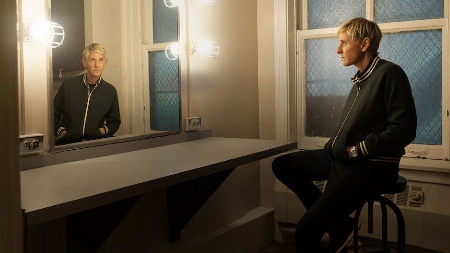 Imagen promocional: Ellen DeGeneres, pensativa en camerino sencillo con chaqueta verde, mirando a una ventana.