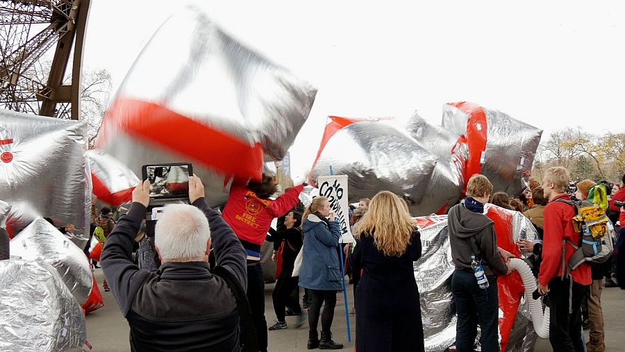 Performance artística con barricadas inflables; un hombre graba la escena con un móvil; varias personas participan en la acción.