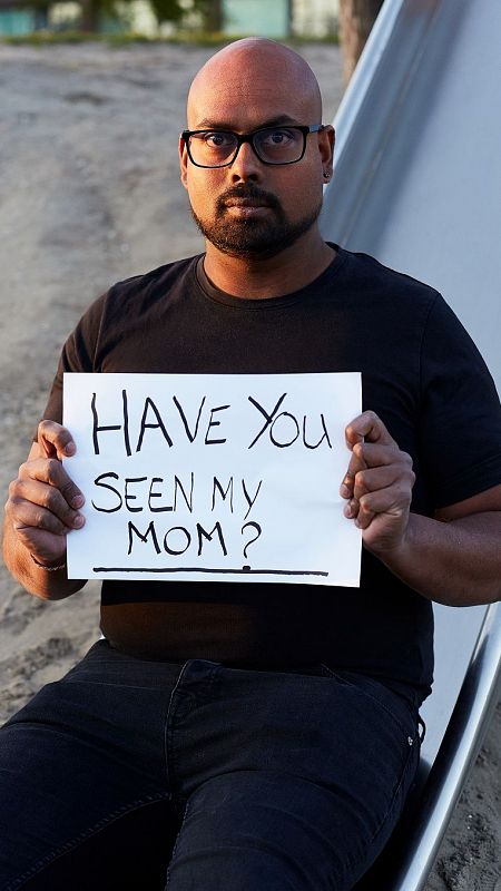 An adoptee holds up a sign that reads: Have you seen my mother?