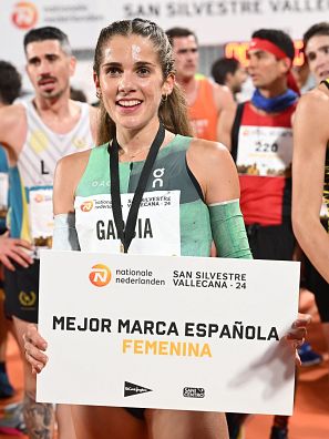 Atleta sonriente con medalla, cartel de la San Silvestre Vallecana y camiseta con su apellido.  Mejor marca española femenina.