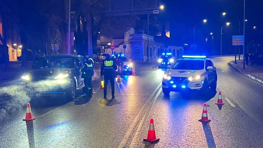 Control policial de Nochevieja en Ciudad Real. Agentes de la Policía Local inspeccionan un vehículo detenido, con apoyo de coches patrulla y conos de tráfico.  Vapor sale del tubo de escape del coche.