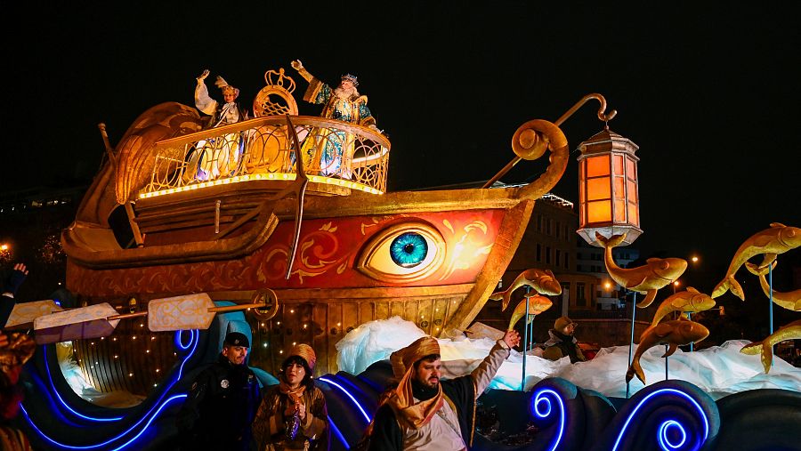 Carroza con forma de barco, iluminada y decorada con motivos marinos, en la cabalgata de Reyes Magos.  Los Reyes Magos saludan desde ella.