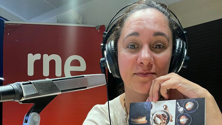 Beatriz Cano en estudio de radio, con auriculares y micrófono, sosteniendo una tarjeta con imágenes de comida.  Expresión seria, posible noticia cultural.