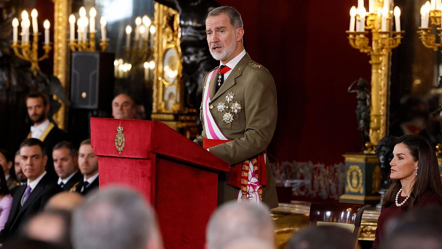 El Rey Felipe VI, en uniforme militar, ofrece un discurso en un salón palaciego durante la Pascua Militar; la Reina Letizia le escucha.