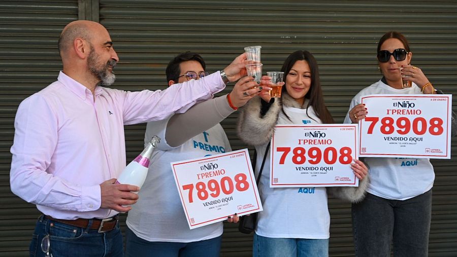 Celebración en una administración de lotería por la venta del 1º premio de la Lotería del Niño 2025 (78908). Cuatro personas brindan con champán.