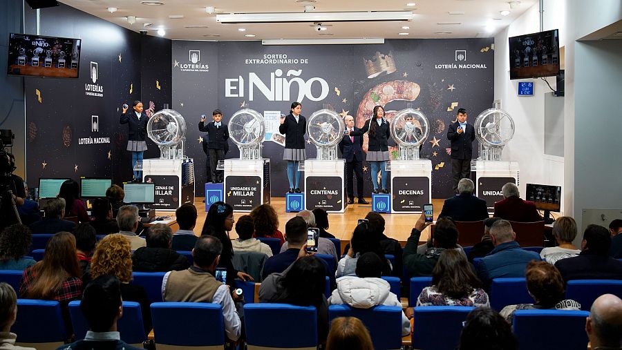 Niños extraen bolas de los bombos en el Sorteo de la Lotería del Niño 2025, ante un público que fotografía el evento.