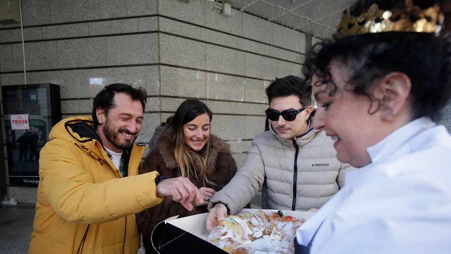 Alegría y celebración por un premio de lotería: tres personas disfrutan de un roscón de Reyes.  Un número parcialmente visible (76908) se ve al fondo.