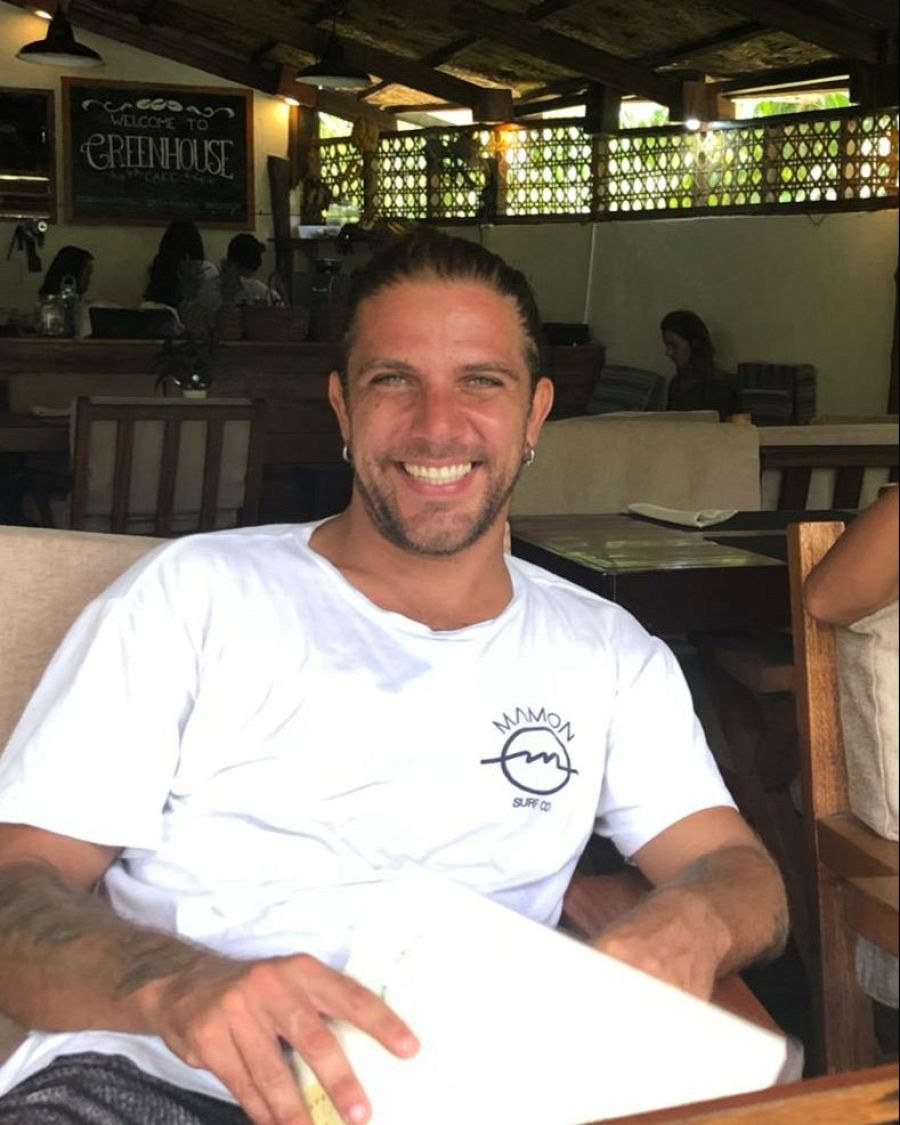 Diego Bello, de Mamon Surf Co., sonríe en una foto tomada en el restaurante Greenhouse. Lleva una camiseta blanca con el logo de su marca.