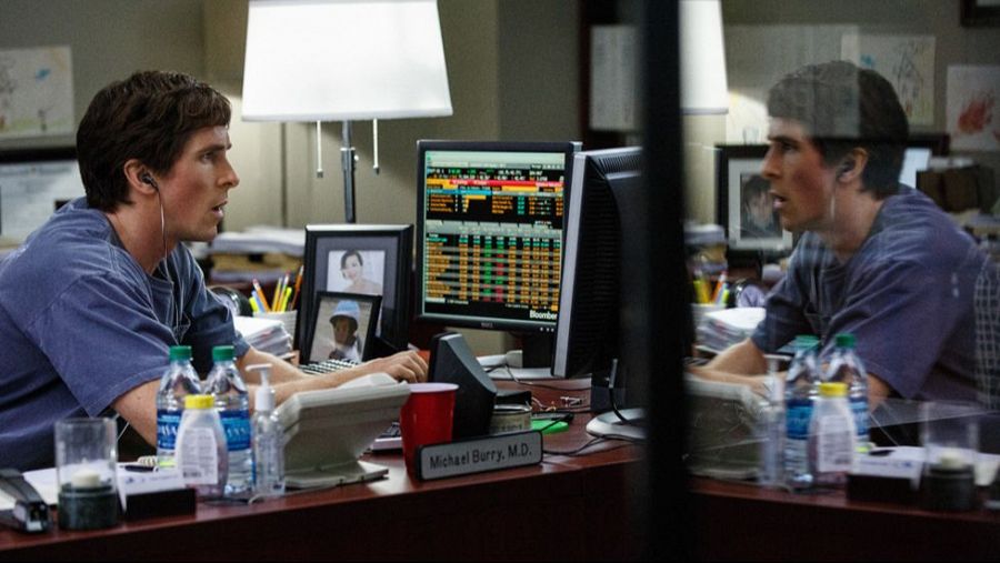 Christian Bale interpreta a Michael Burry en una escena de oficina de 'La gran apuesta'.  Se le ve concentrado en su trabajo con auriculares, rodeado de monitores, papeles y objetos personales.