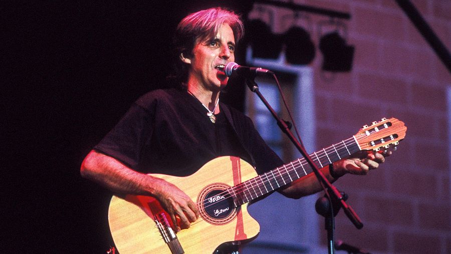 Kiko Veneno en concierto de 1992: canta y toca una guitarra acústica de color claro con detalles rojos, con una iluminación tenue y rojiza de fondo.