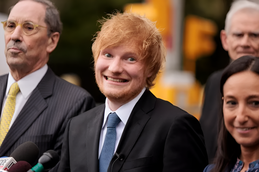 Ed Sheeran, sonriente y con traje oscuro, posa con su equipo legal tras una aparente victoria.  Un hombre con gafas y traje observa seriamente.  Varios micrófonos sugieren una conferencia de prensa.