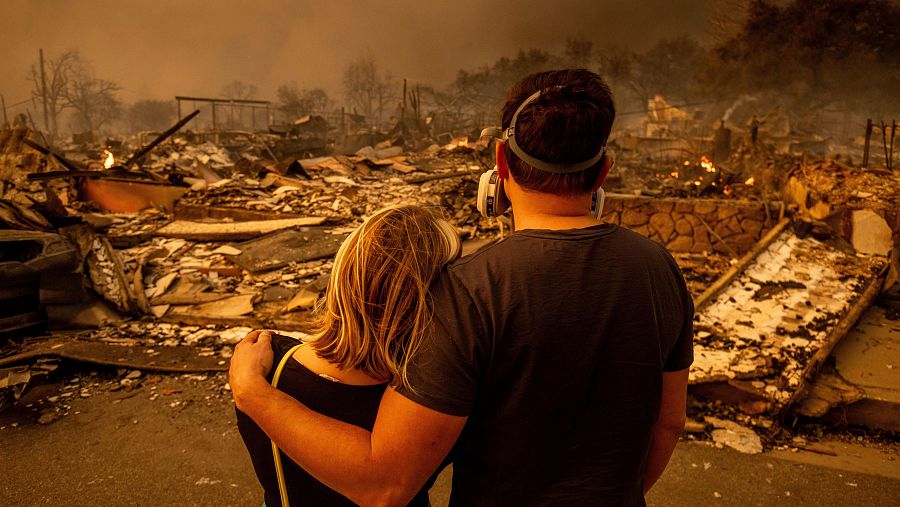 Dos personas se abrazan frente a los restos de una casa dañada por el incendio en Altadena, California