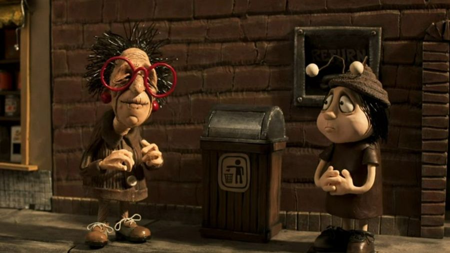 Dos personajes de plastilina, una anciana con gafas y un niño con antenas, interactúan en una calle con una papelera y una señal 'RETURN'.  Escena de animación.