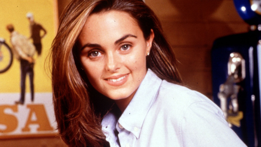 Retrato de Carmen Morales con camisa clara, pelo castaño y sonrisa; fondo con cabina telefónica azul y cartel amarillo con bicicleta.