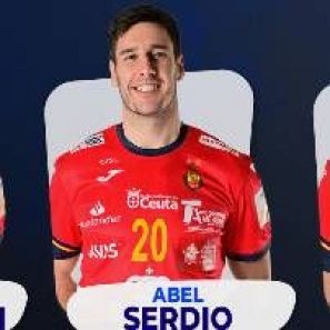 Jugador de balonmano con camiseta roja número 20, nombre en la camiseta y varios logotipos de patrocinadores. Sonríe, fondo azul oscuro.