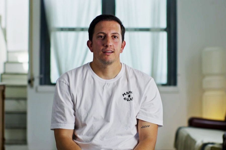 Retrato de un hombre con camiseta blanca, sentado en una habitación con ventana.  Expresión seria.  Mensaje: 