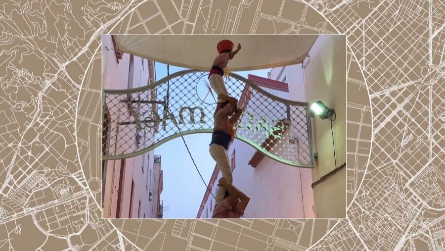 Torre humana con cuatro participantes, uno con camisa roja en la cima, construida bajo un arco metálico en una calle.