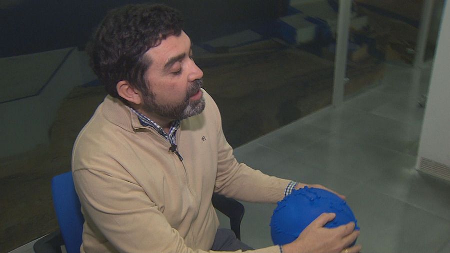 Astrofísico invidente con barba y cabello oscuro estudia el universo con una esfera azul táctil que proporciona información astronómica a través del tacto y el sonido.