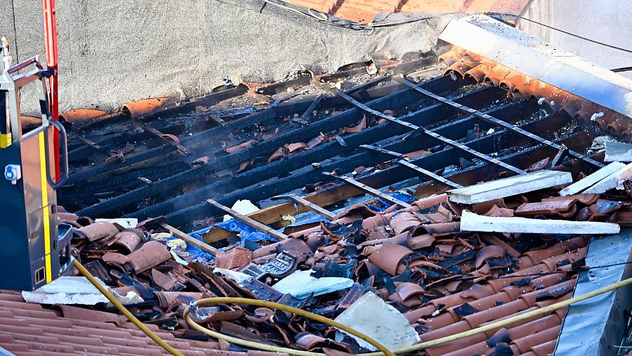 Tejado dañado por incendio: tejas rotas, vigas ennegrecidas y escombros.  Presencia de manguera de bomberos.