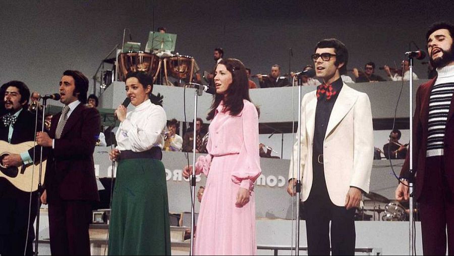Actuación de Mocedades en Eurovisión: seis cantantes (tres hombres, tres mujeres), dos con guitarras, frente a una orquesta. Vestuario años 70.
