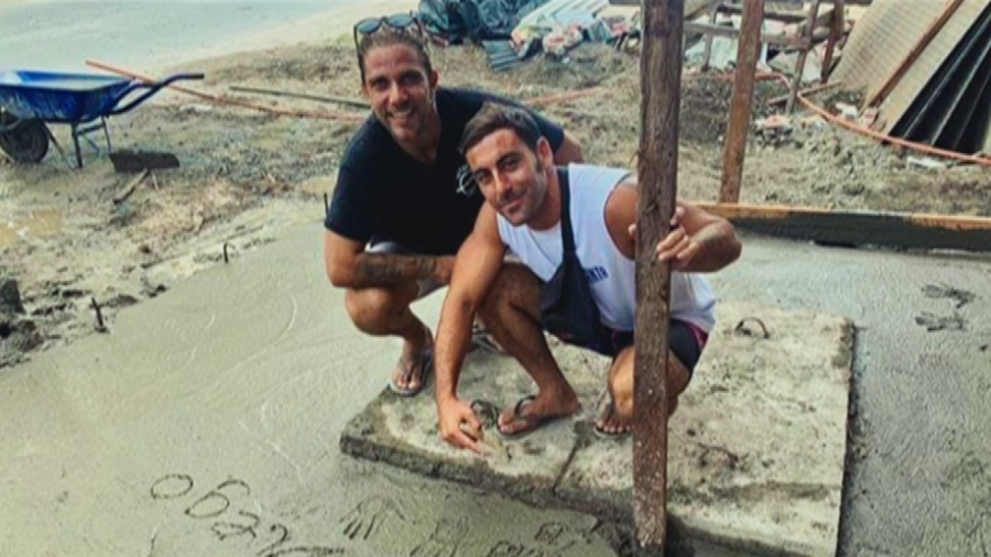 Dos hombres agachados en una obra, uno señala una fecha (