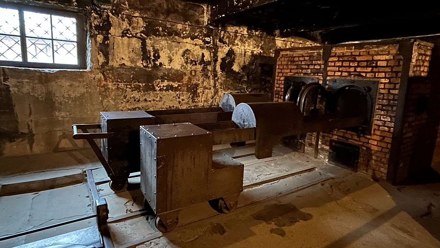 Interior de crematorio de Auschwitz: dos vagones oxidados para cadáveres, hornos de ladrillo y ambiente sombrío.