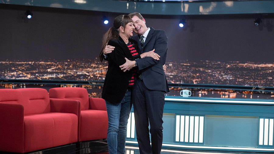 Yolanda Ramos y Marc Giró se abrazan en el plató de Late Xou. Ella viste chaqueta negra y vaqueros; él, traje azul marino.  Ambiente cordial.