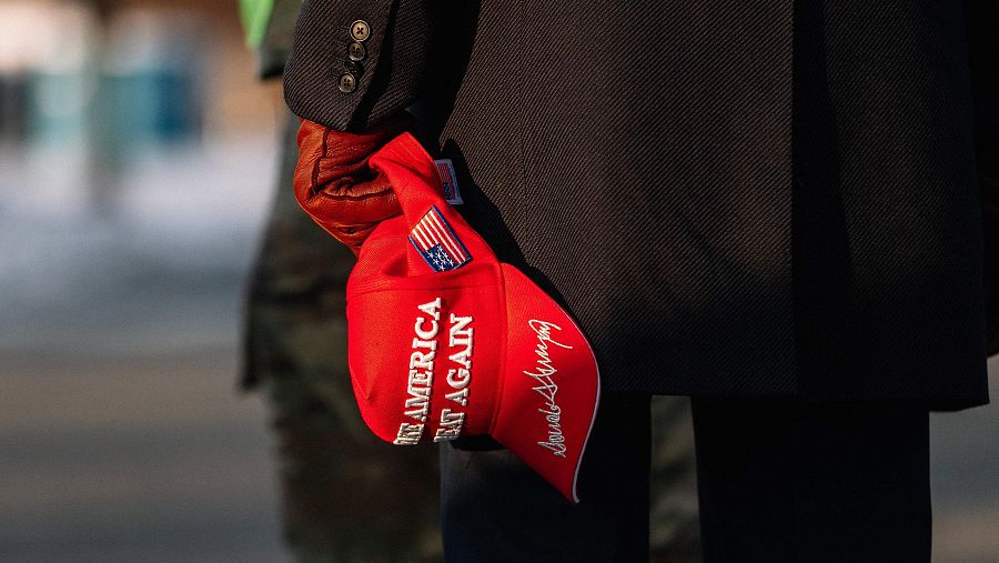 Hombre con gorra roja 'Make America Great Again' frente al Capitolio.  Apoyo a Trump antes de investidura presidencial.  Posible alusión a elecciones 2024.