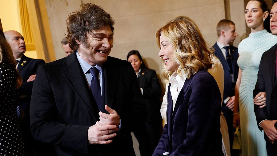 Reunión entre Javier Milei y Giorgia Meloni; ambos líderes, vestidos formalmente, conversan de manera relajada y sonriente en un ambiente interior.